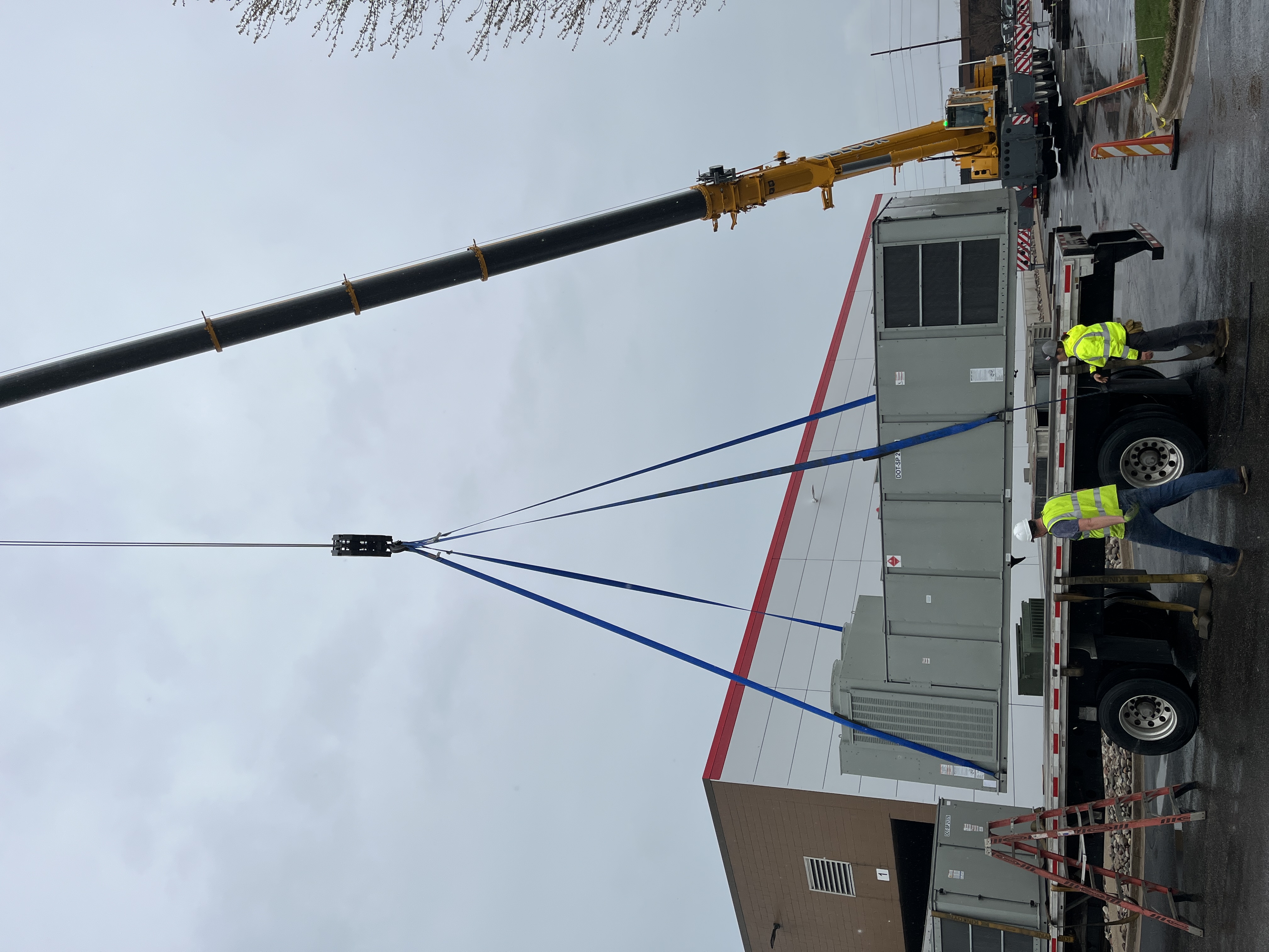 Crane lifting new industrial rooftop HVAC unit onto Holland, MI metal stamping plant